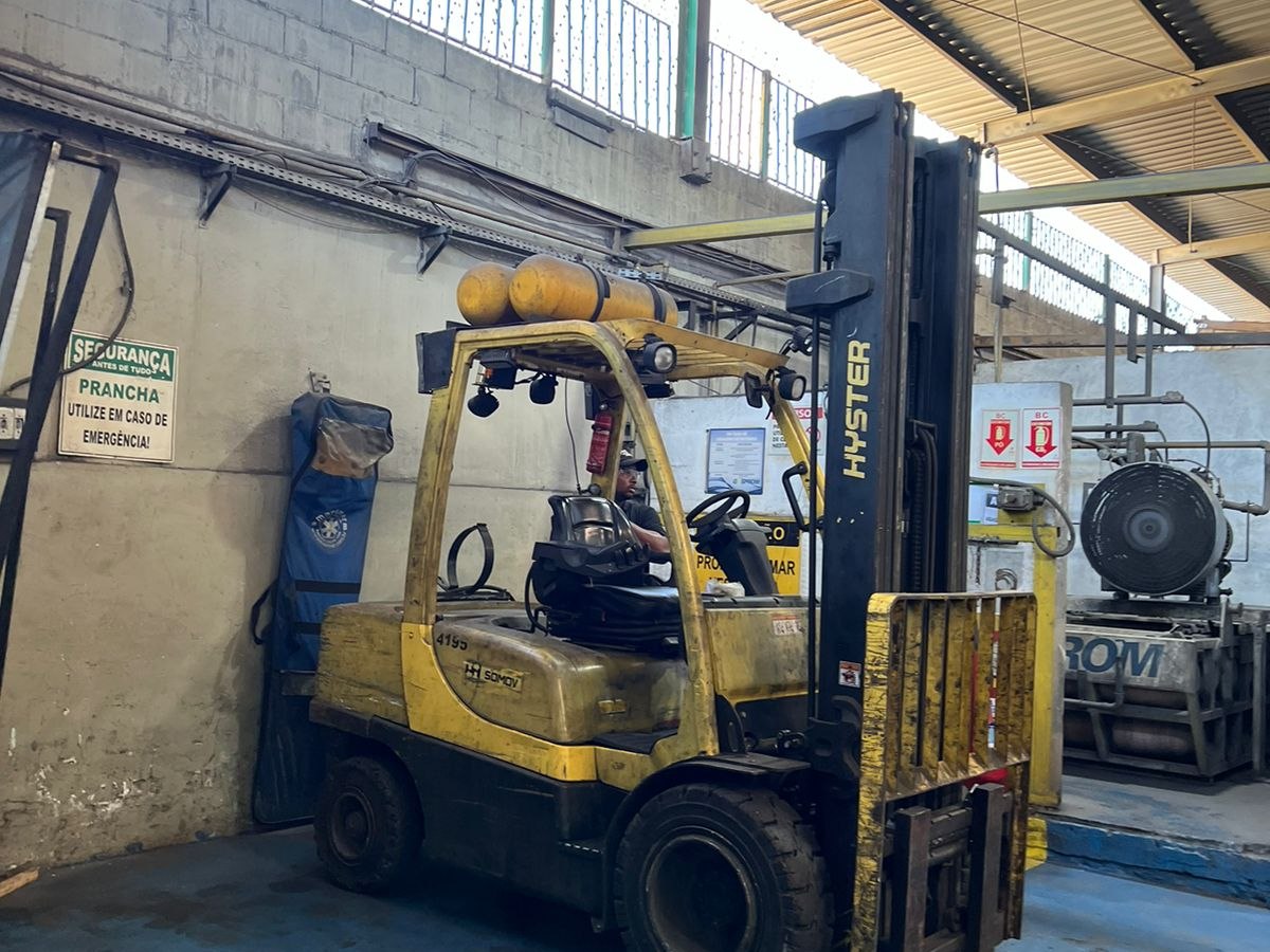 Empilhadeira convertida para GNV com cilindros de gás natural no teto operando em galpão industrial com compressor Gasprom ao fundo
