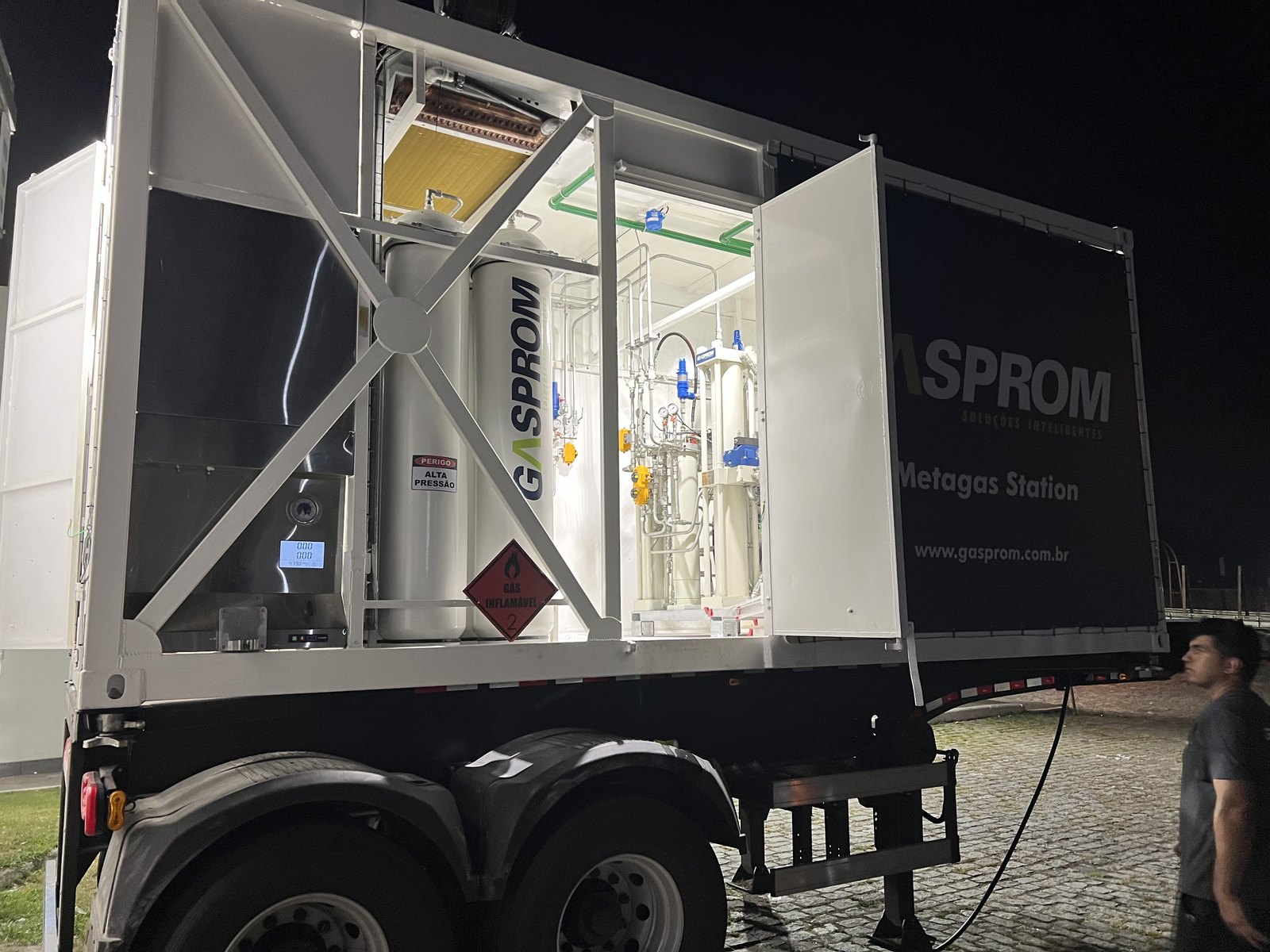 Metagas Station Gasprom com portas abertas à noite mostrando cilindros de armazenagem e painel de compressão iluminados